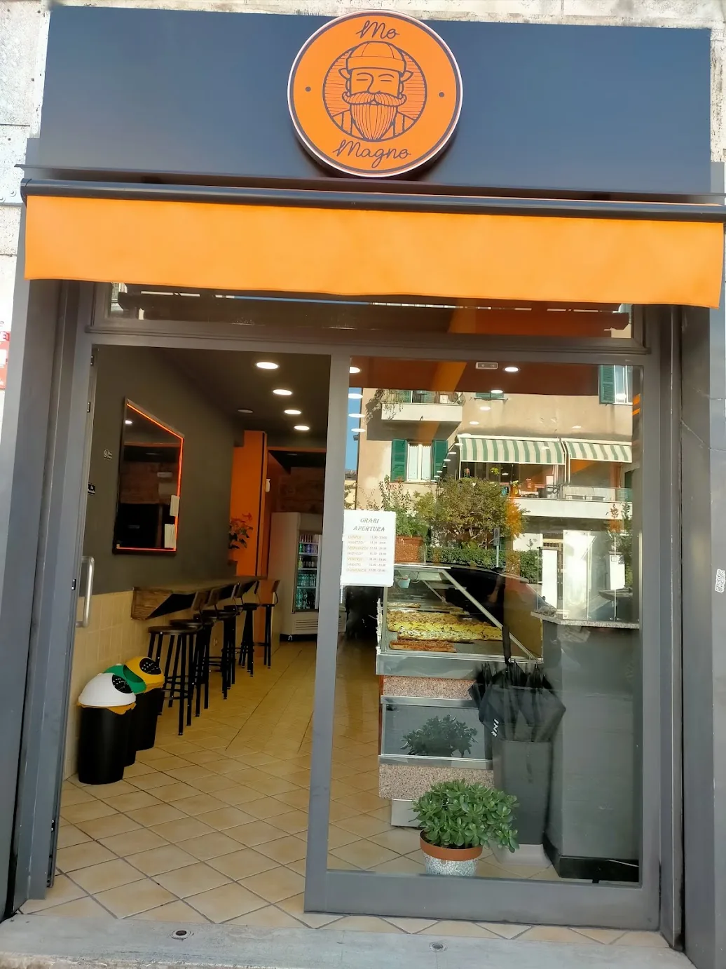 L'ingresso di Mo Magno in Via dei Gelsi: insegna col logo, tenda arancione e vetrina